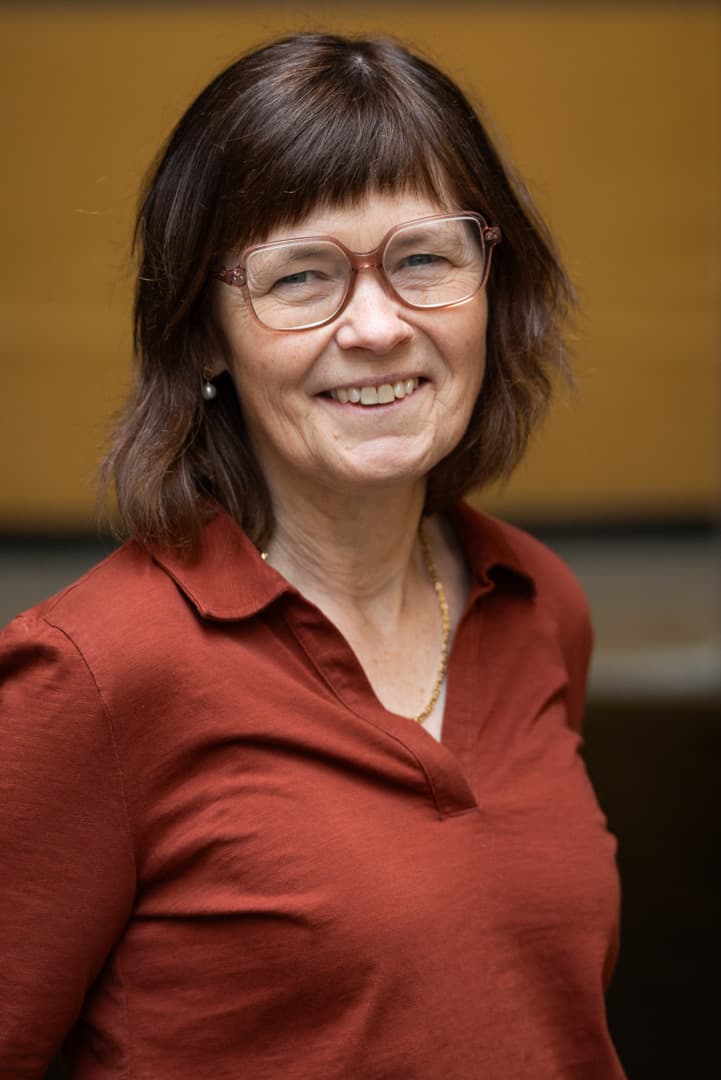 Elisabeth har på rød skjorte og ser inn i kameraet og smiler.