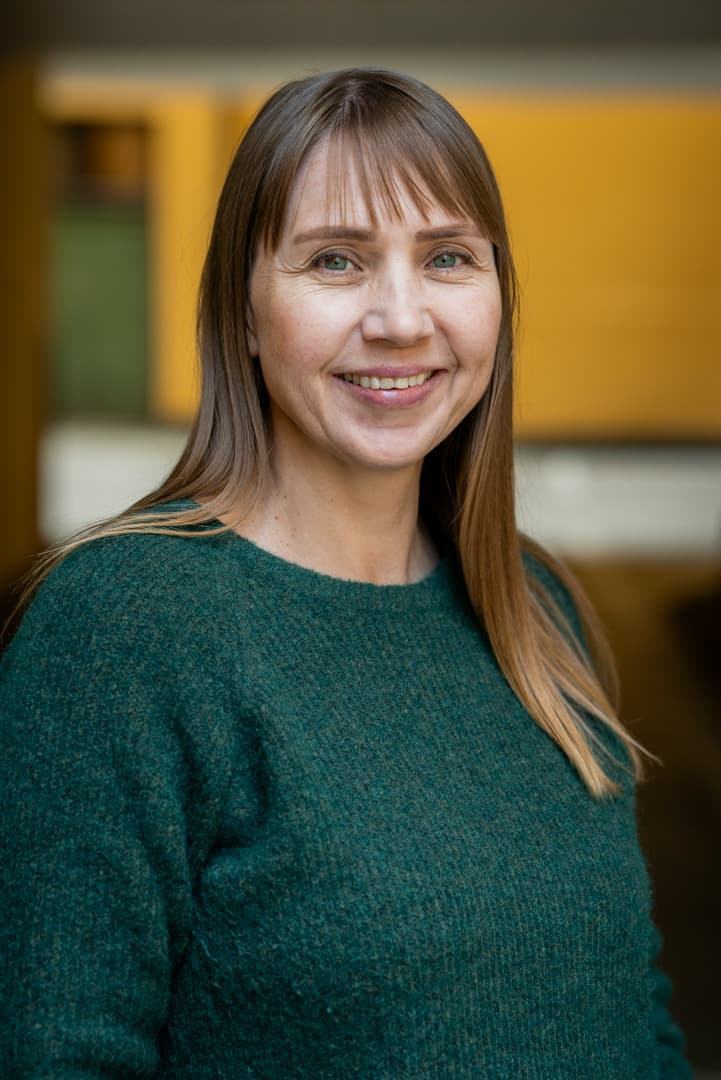 Lill har på grønn genser og ser inn i kamerat og smiler.