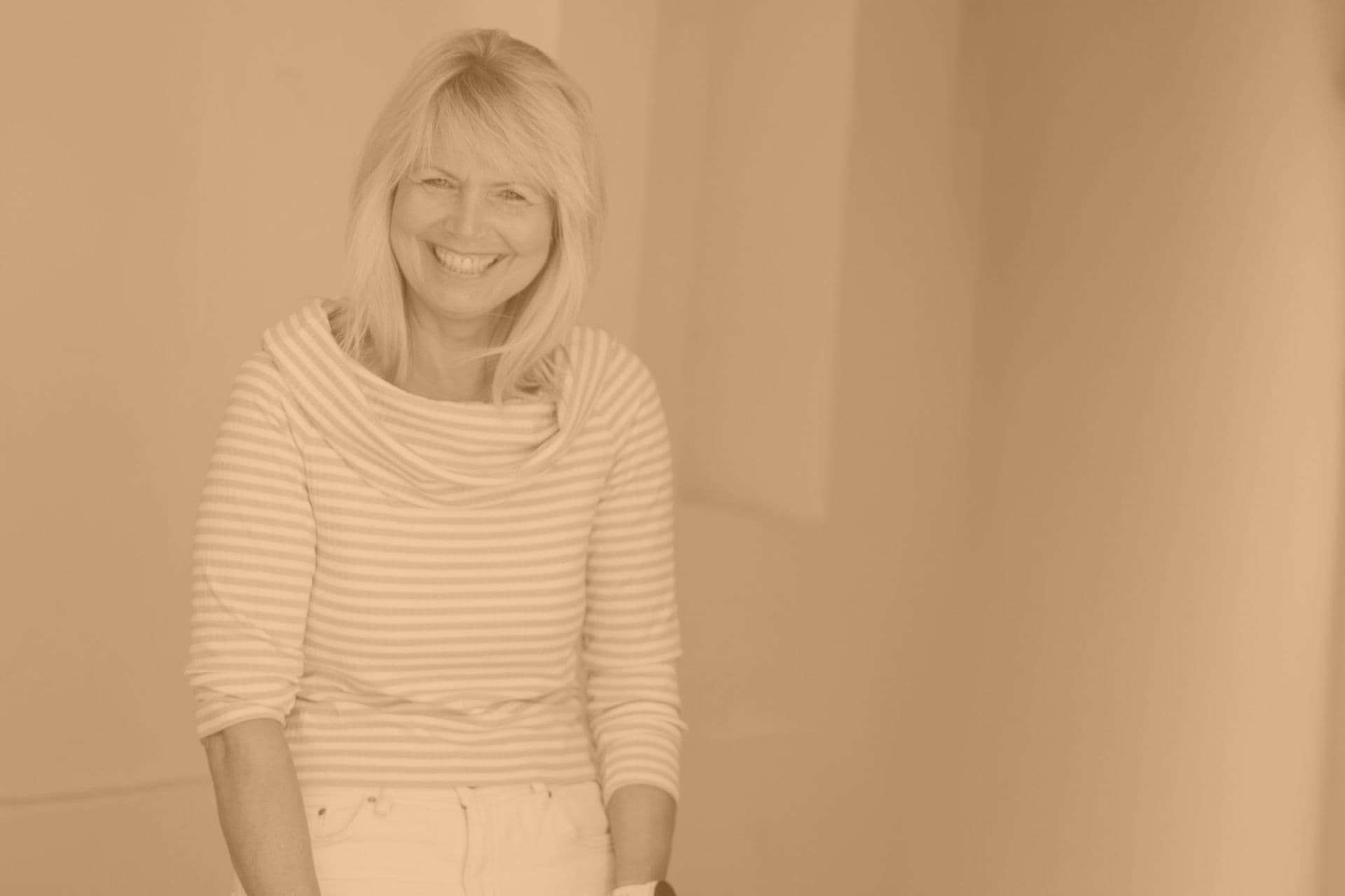 Kvinne ler mens hun ser inn i kameraet. Oransje, sepia-aktig filter over bildet.